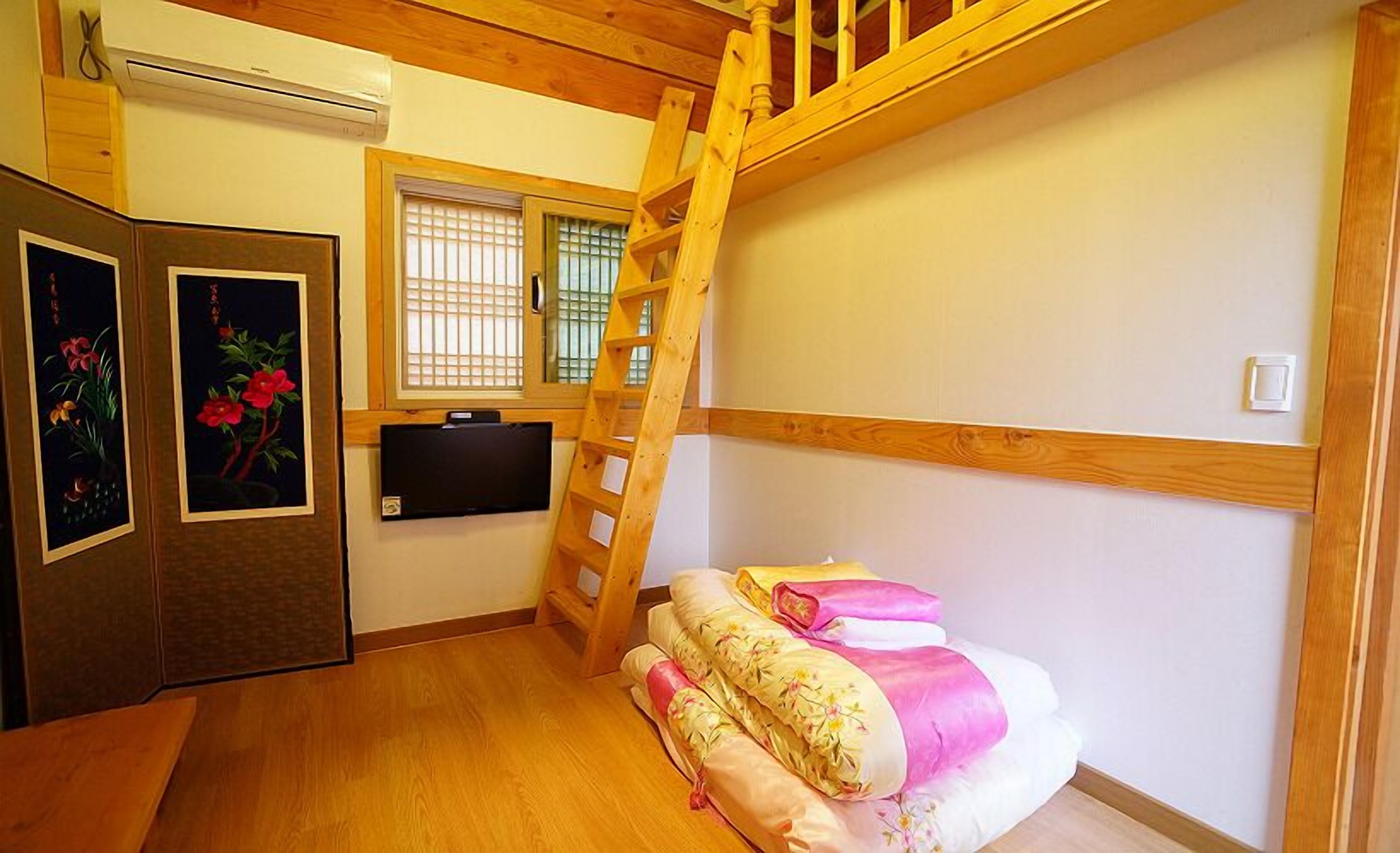 A small room with a bunk bed, a wooden ladder, a TV, and a window with blinds.