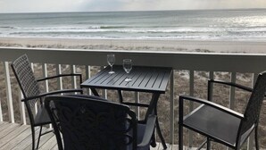 Eine Holzterrasse mit zwei Stühlen und einem Tisch, mit Blick auf einen Strand, Wellen und einen bewölkten Himmel.