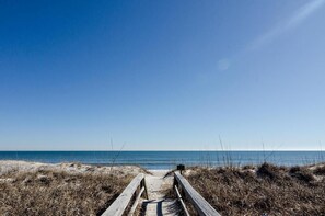 Un muelle de madera que conduce a una playa, con cielos despejados.