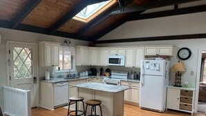 A kitchen with wooden beams, white cabinets, a central island with stools, a microwave, stove, and refrigerator. - Great Vacation Destination, 1 Mile To Storyland, Skiing, Golf, Hiking. (Bartlett)