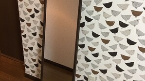 Un miroir avec un cadre noir, accroché à un mur recouvert d’un papier peint à motifs d’oiseaux.