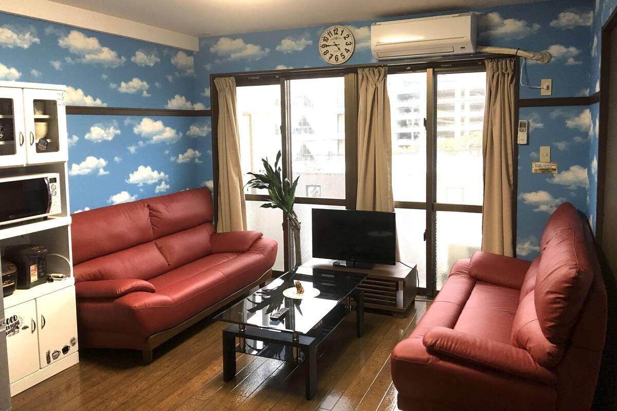 A living room with a red sofa, a glass coffee table, a TV, and a kitchenette with a microwave.