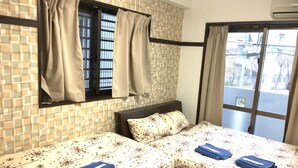 Une chambre d’hôtel avec deux lits, des rideaux de couleur beige, une fenêtre donnant sur la rue et une couvre-lit à motifs.
