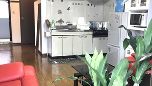 Une cuisine compacte avec des meubles blancs, un réfrigérateur, un four à micro-ondes et un évier. Le salon est agrémenté d’un canapé rouge et d’une plante en pot.
