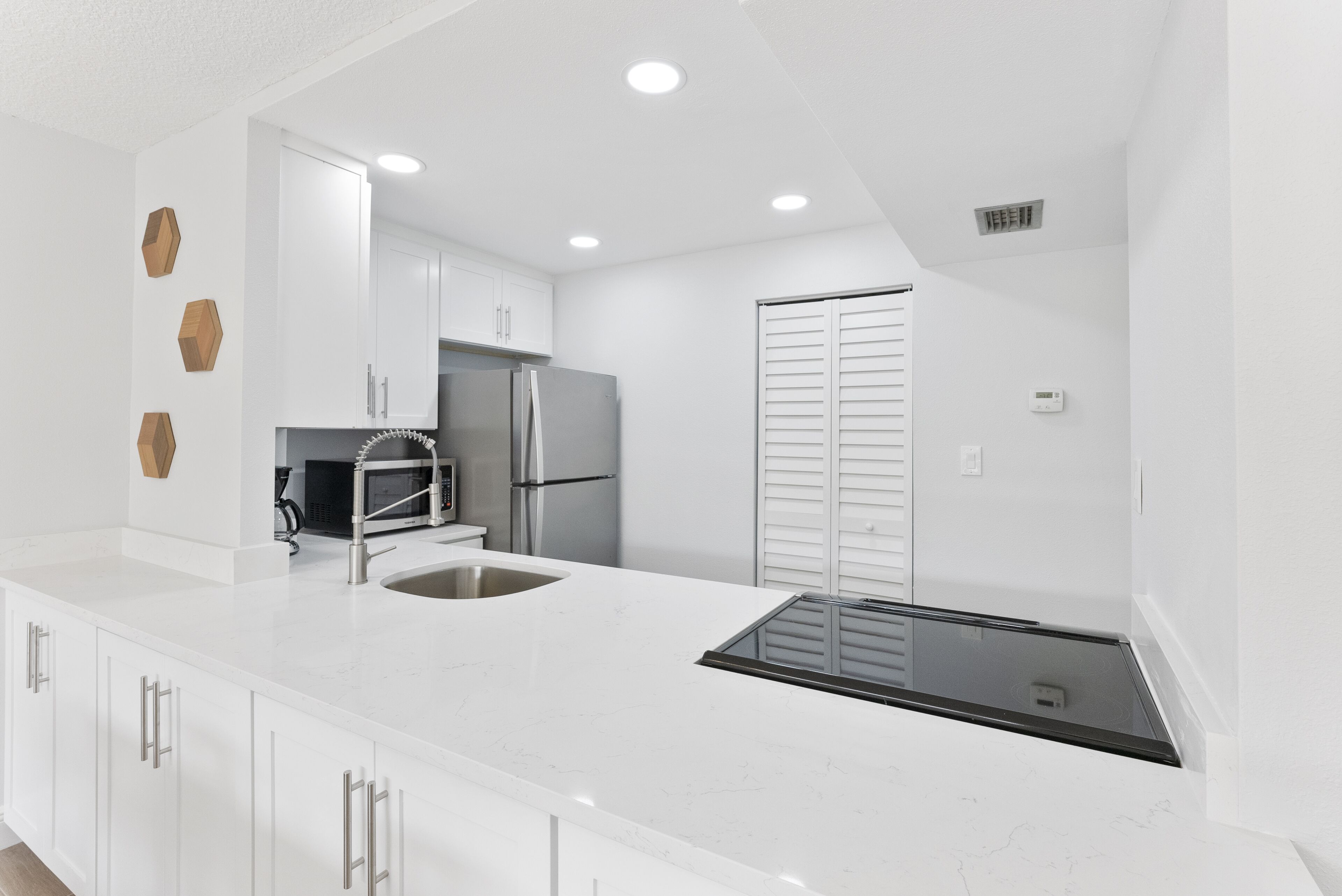 A modern kitchen with white cabinetry, a stainless steel refrigerator, and a black induction cooktop.