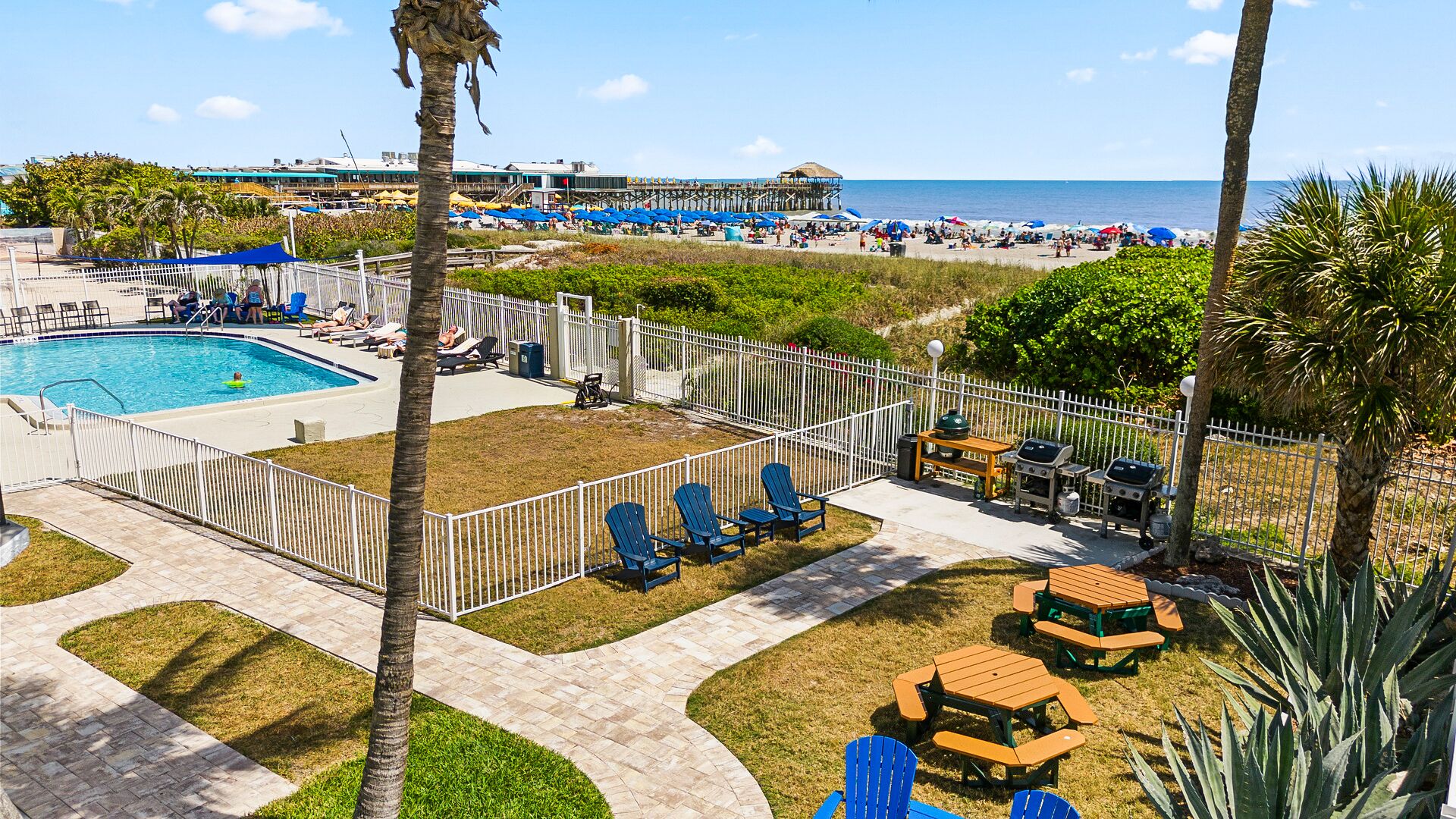 A pool area with lounge chairs, a barbecue setup, and a view of the beach.