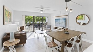 Un salon moderne avec une table à manger en bois, des chaises blanches, un canapé marron et un ventilateur de plafond.