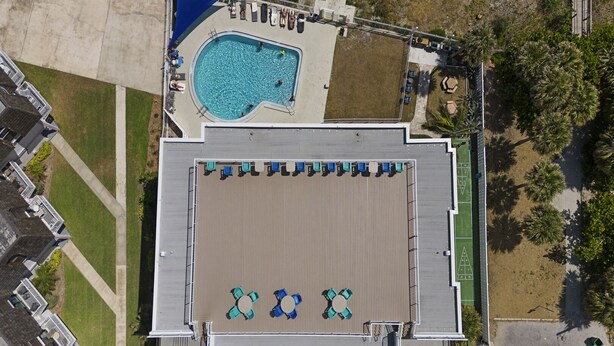Vue aérienne d’un bâtiment doté d’une piscine, d’un espace de détente extérieur et d’un court de tennis.