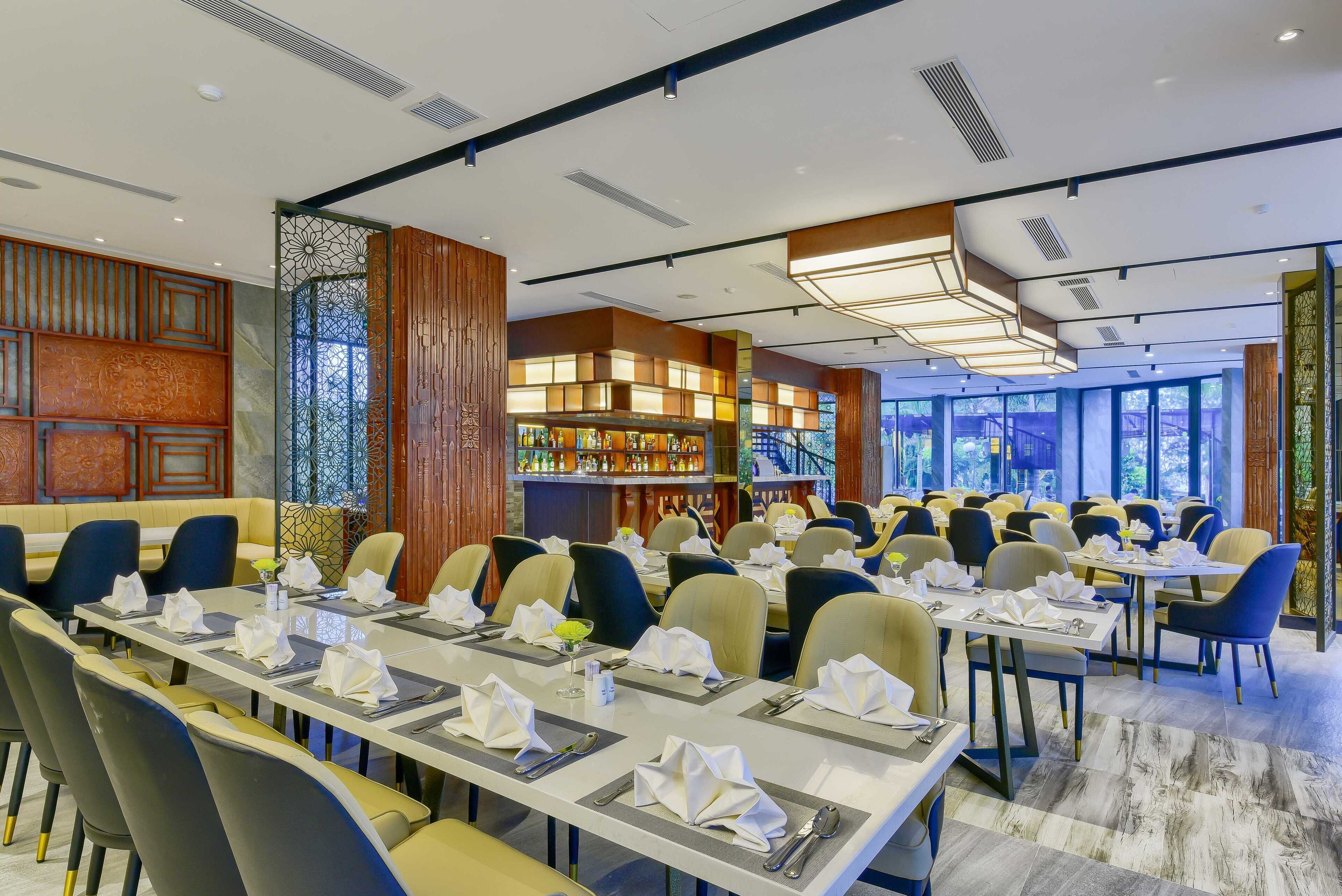 A restaurant with long tables set for dining, a bar area, and a view of the outdoors.