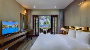 A hotel room with a bed, a desk with a TV, a balcony with a view of the sea, and a table with chairs. - Manli Resort Quang Binh (Dong Thuan)