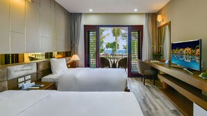 A hotel room with two beds, a desk with a TV, and a balcony with a view of the sea. - Manli Resort Quang Binh (Dong Thuan)
