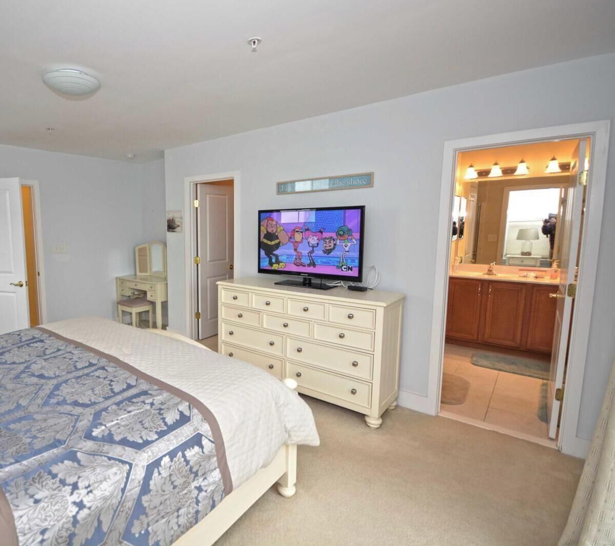 Een kamer met drie slaapkamers, een bed, een dressoir, een televisie en een badkamer die door een geopende deur zichtbaar is.
