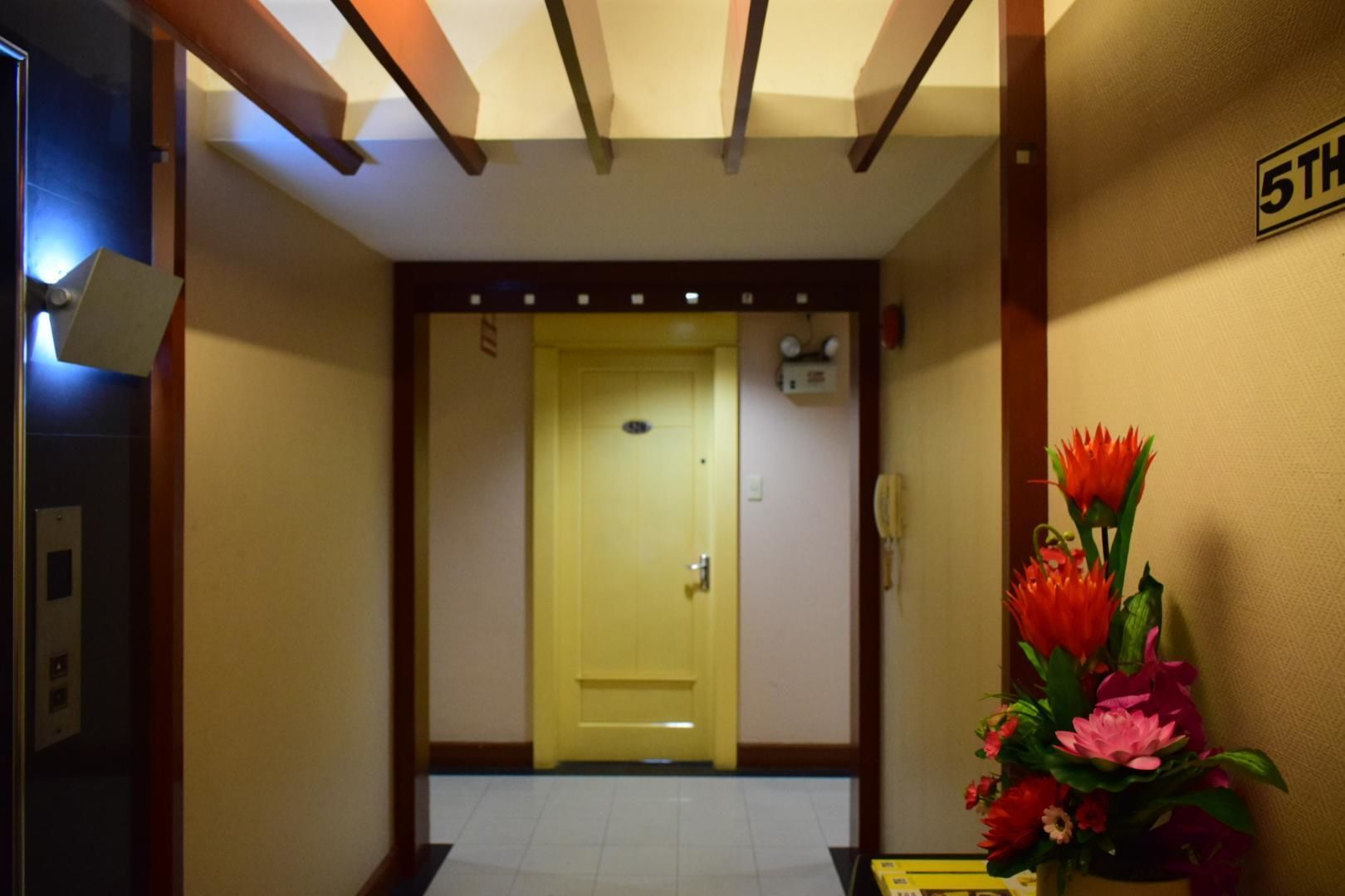A hallway with a yellow door, a telephone, and a flower arrangement.