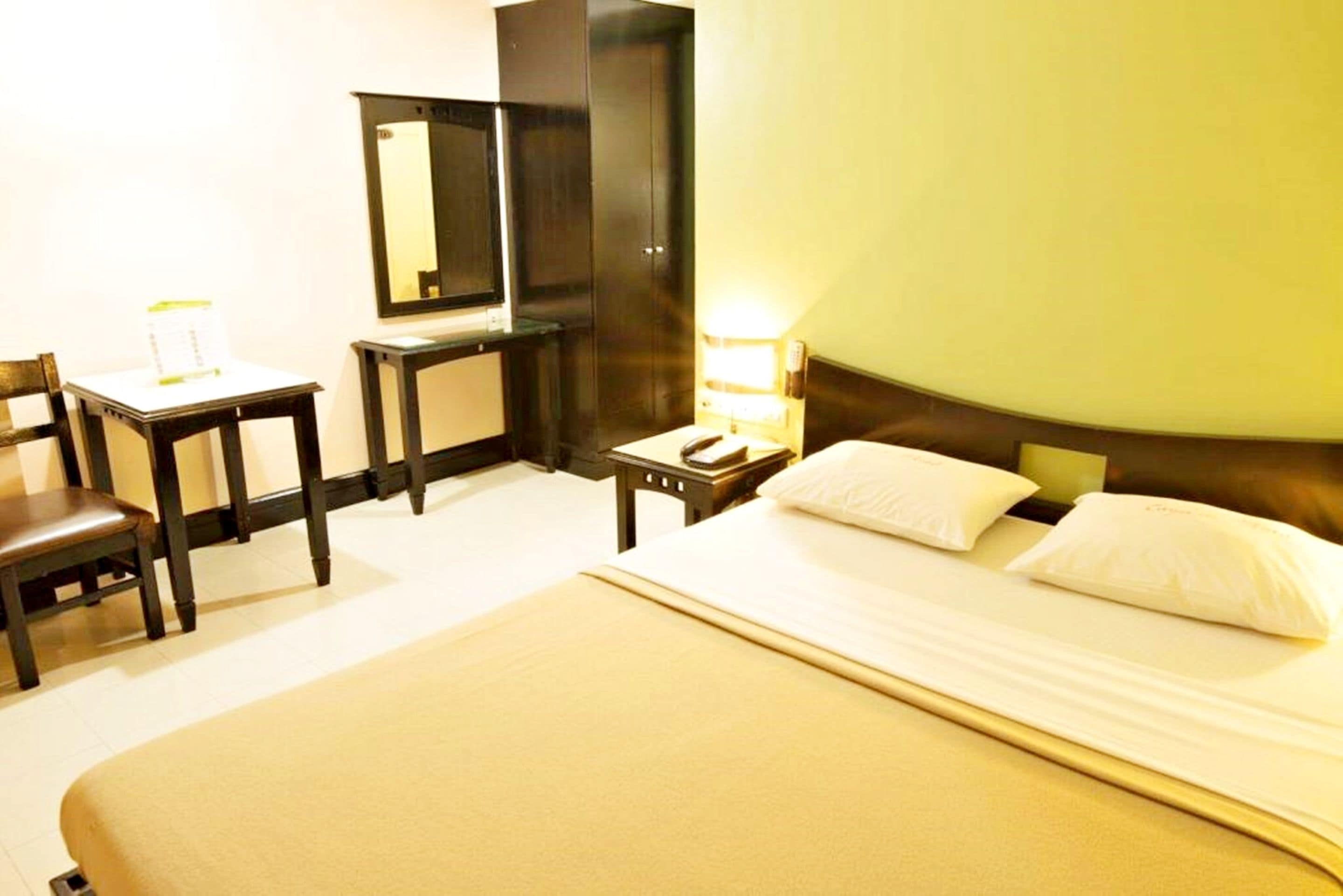 A hotel room with a bed, a desk, a chair, a nightstand, and a mirror.