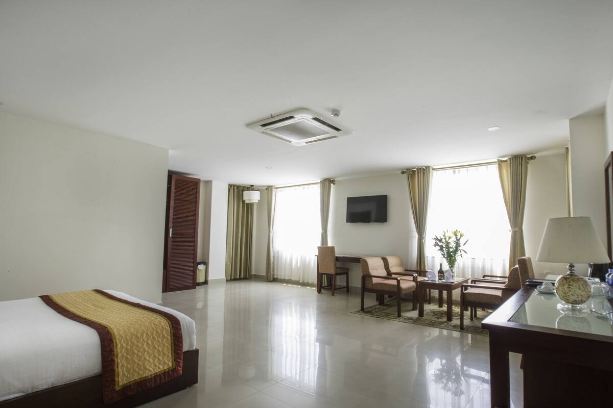Habitación de hotel con cama, escritorio, silla, televisor y ventana con cortinas.