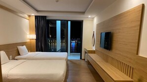 A hotel room with two beds, a TV, a bench, and a view of a cityscape at night. - Luxe Hotel (Dong Hoi)