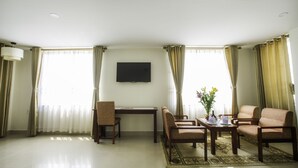 A spacious living room with a flat-screen TV mounted on the wall, a dining table with chairs, and a sofa. - Luxe Hotel (Dong Hoi)