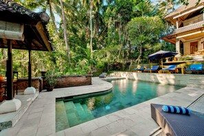 Un espace piscine avec des chaises longues, un coin salon abrité et un jardin en briques.