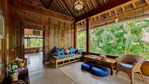 A traditional wooden interior with a sofa, blue cushions, and a wicker chair. - Kebun Indah Ubud (Ubud)