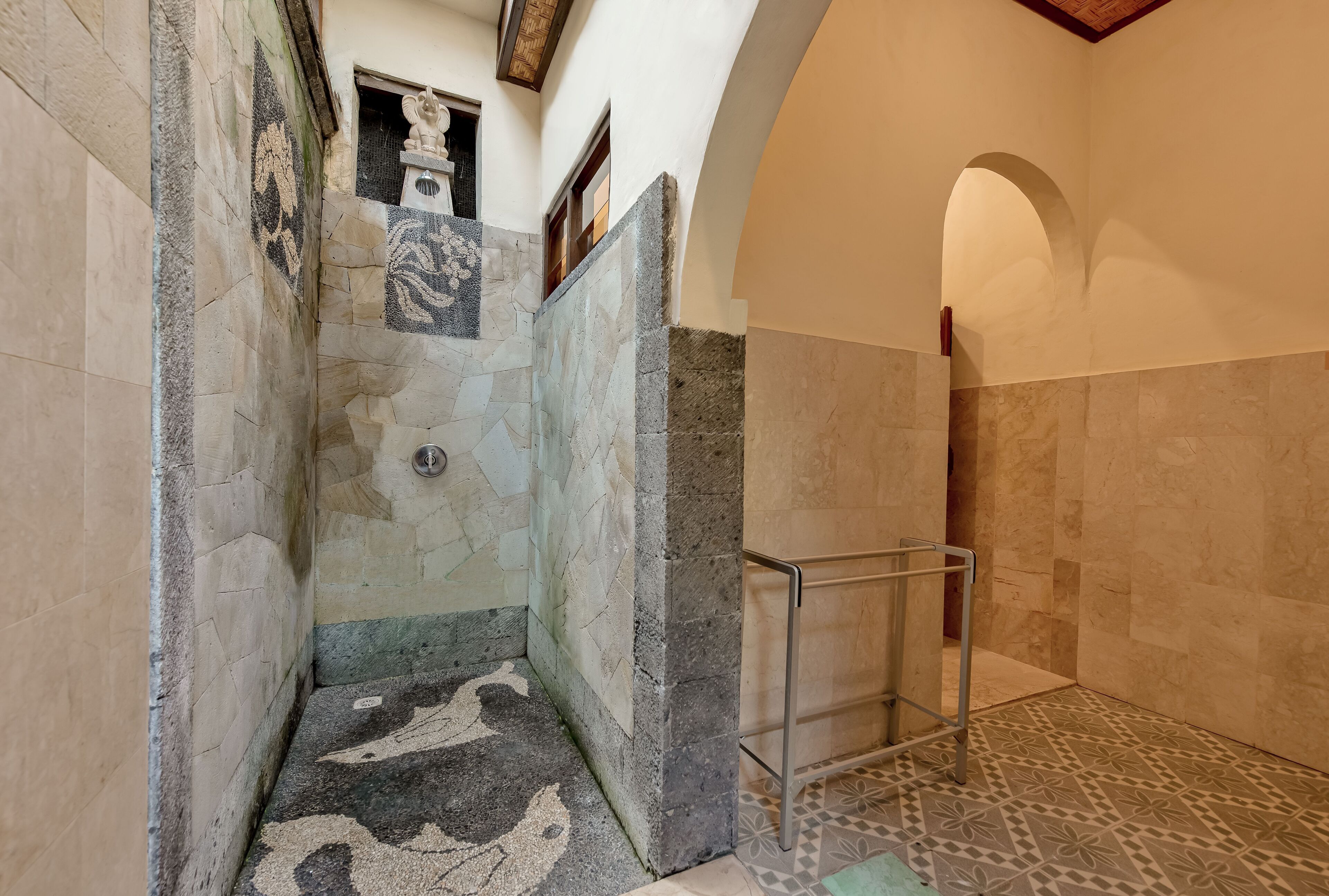Un espace douche doté d’un sol carrelé, d’une barre d’appui en métal et d’un mur en pierre orné d’un motif décoratif.