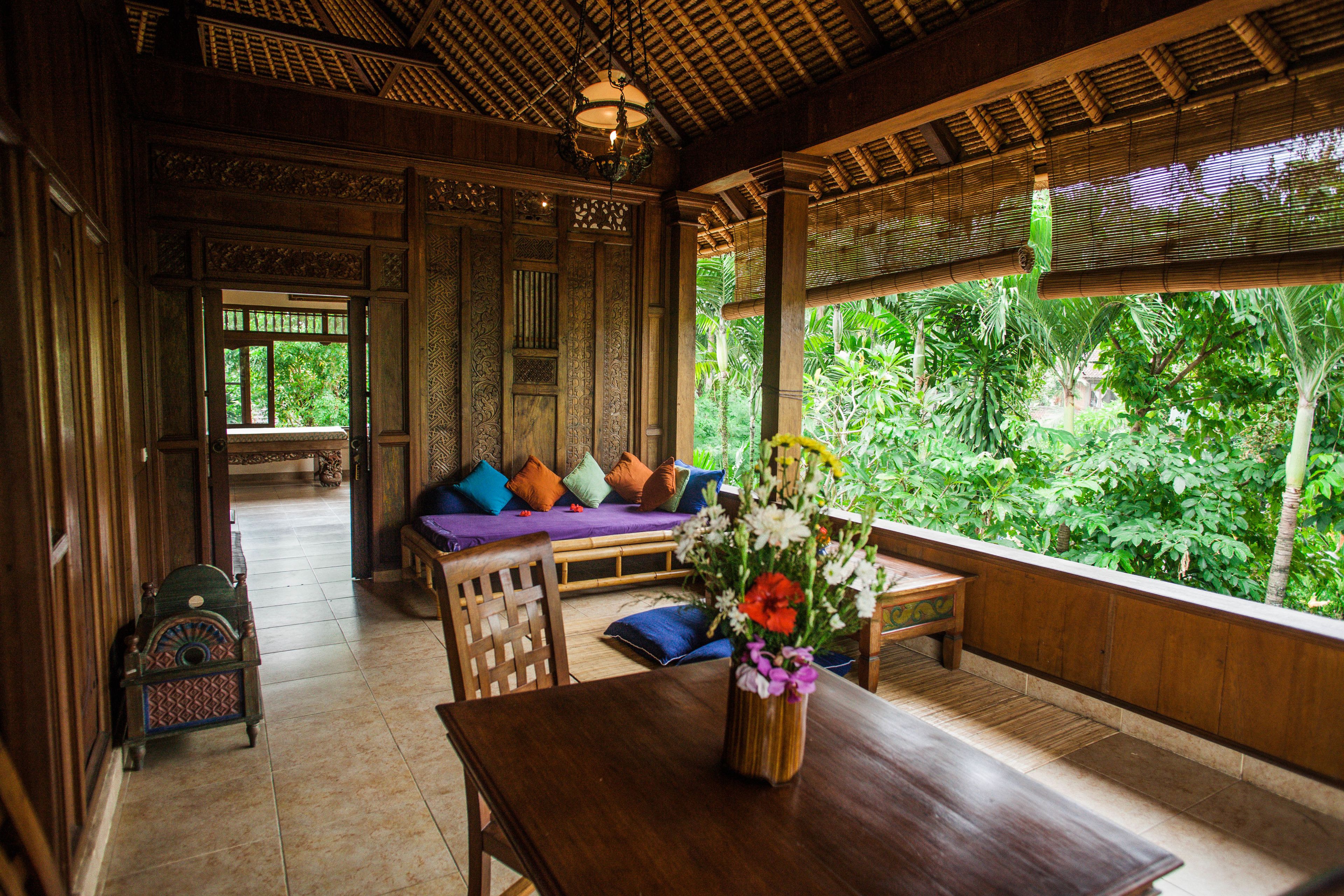 A traditional wooden interior with a sofa, a table, and a view of lush greenery outside.