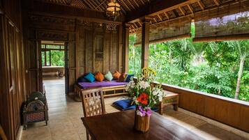A traditional wooden interior with a sofa, a table, and a view of lush greenery outside.