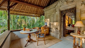 A room with a wooden ceiling, a round table with chairs, a bed with a canopy, and a view of lush greenery outside. - Kebun Indah Ubud (Ubud)