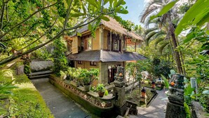 A traditional house with a thatched roof, surrounded by lush greenery and a small garden. - Kebun Indah Ubud (Ubud)