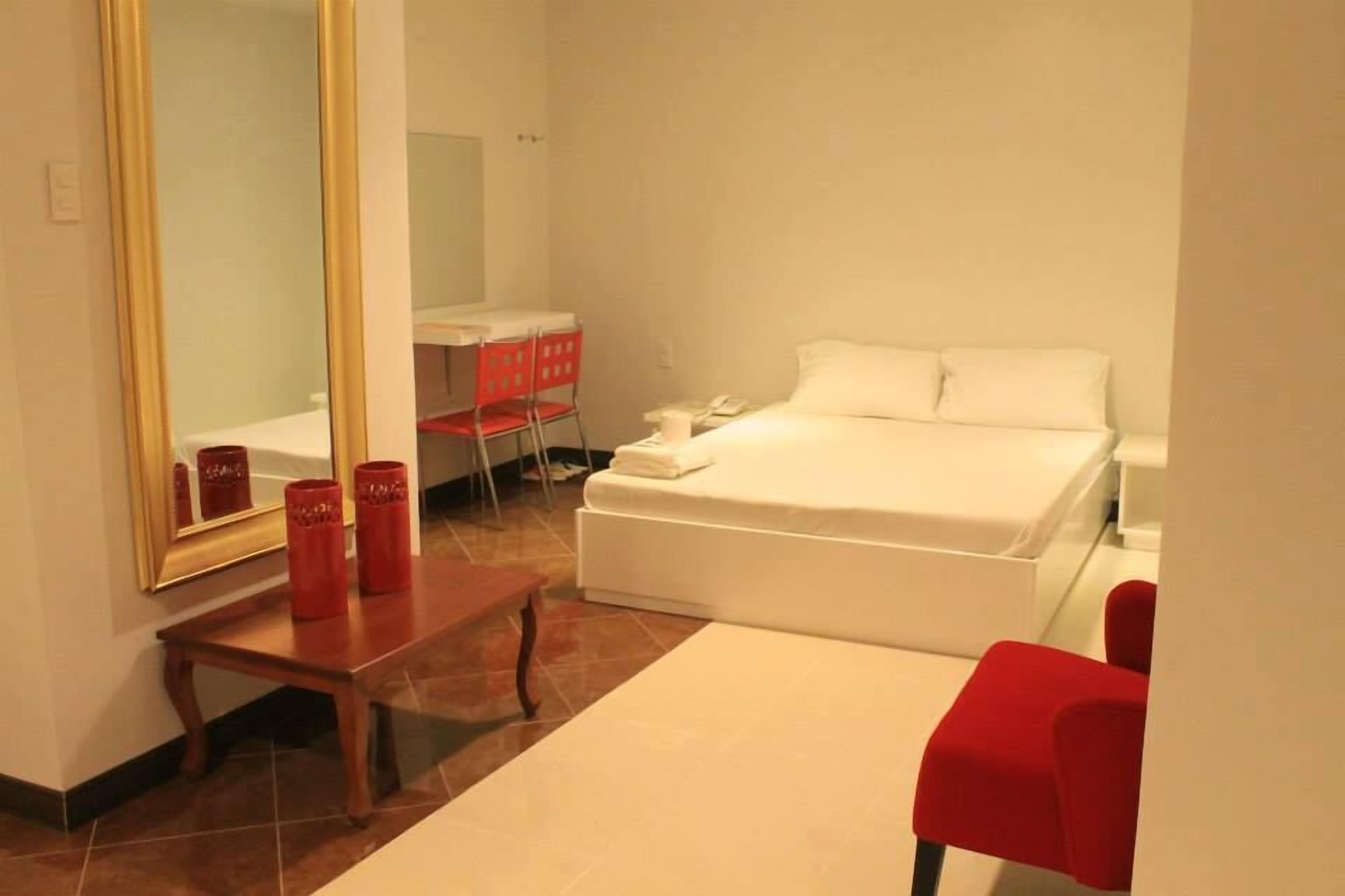 A hotel room with a bed, a desk, a chair, and a mirror.