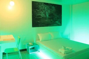 A room with a bed, a nightstand, a chair, and a painting of a waterfall.