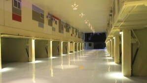 Un largo pasillo bien iluminado con hileras de columnas y un suelo brillante, que conduce a una zona oscura al final.