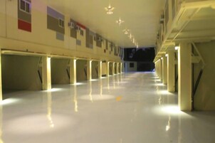 A long, well-lit corridor with rows of columns and a shiny floor, leading to a dark area at the end.