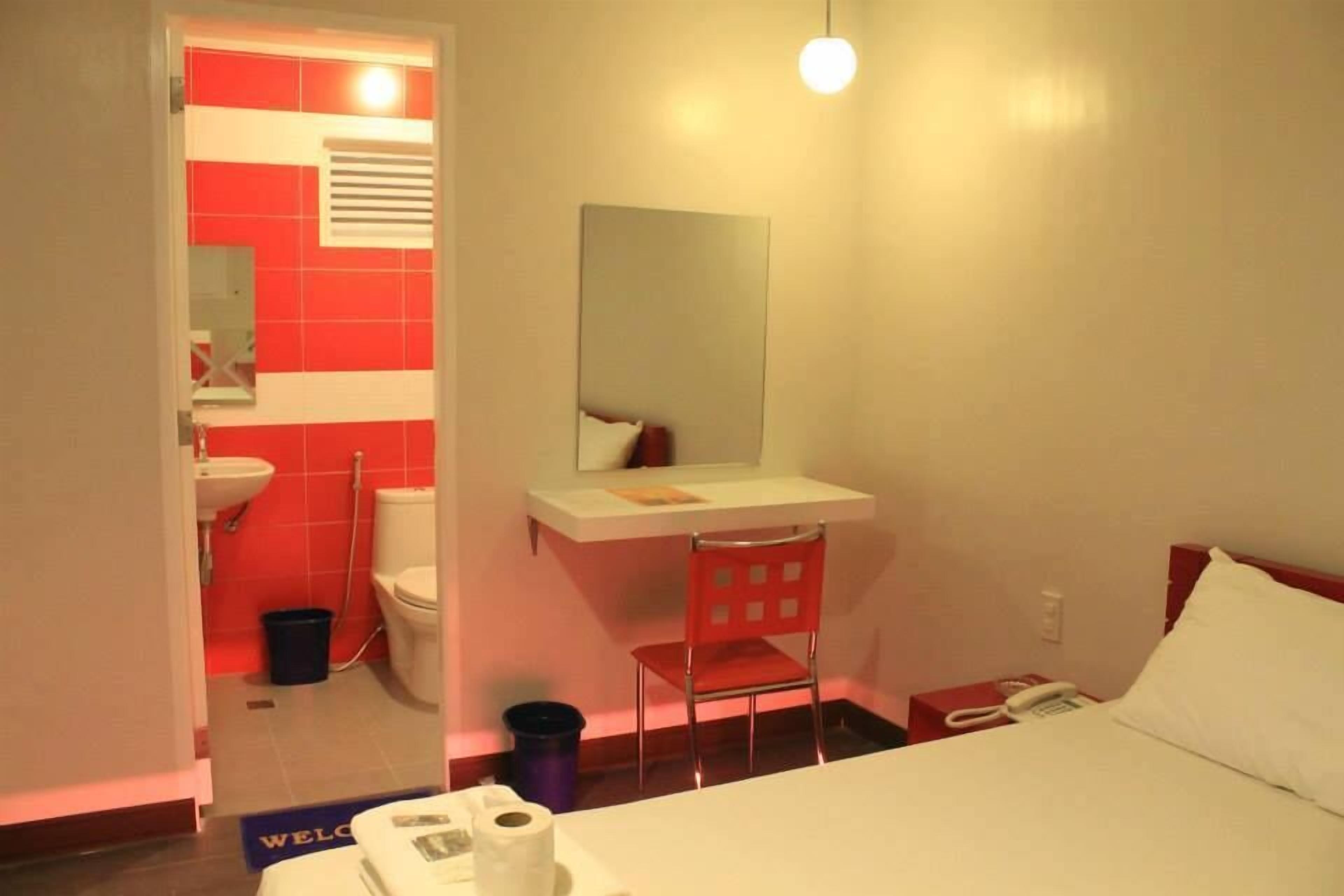 Una habitación de hotel con cama, escritorio, silla, espejo, lavabo e inodoro.
