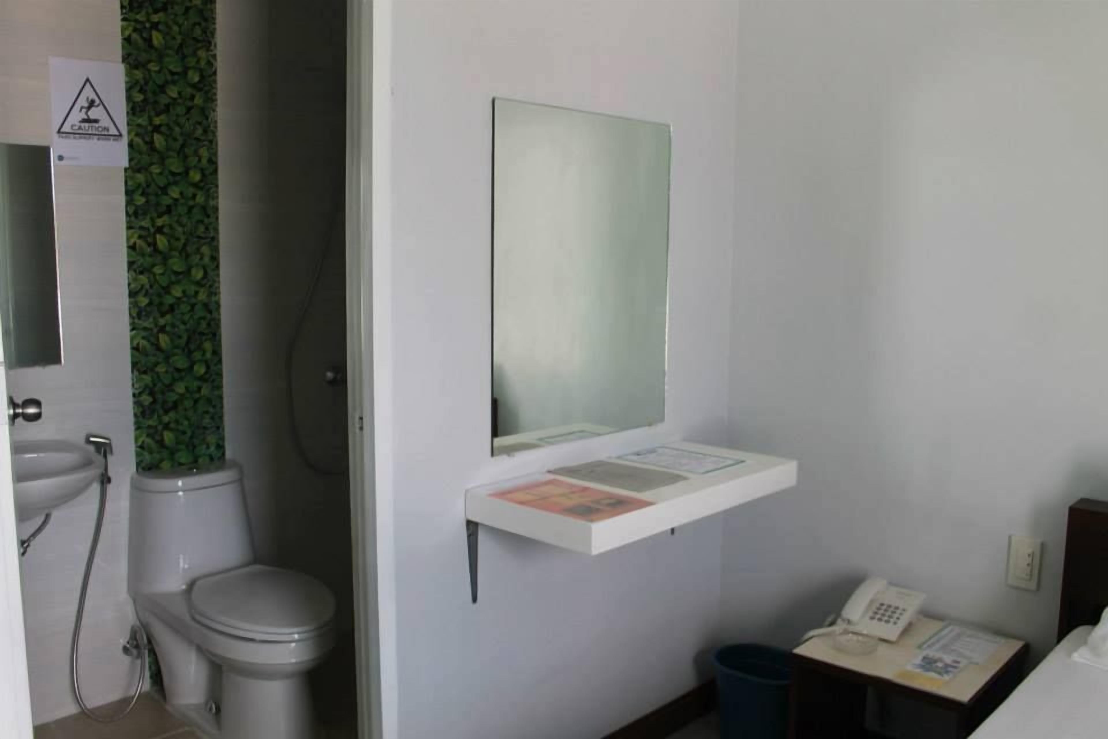 Un baño pequeño con inodoro, lavamanos y un espejo sobre una estantería con un teléfono y documentos.