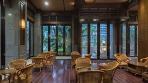 A spacious indoor area with wicker furniture and large windows offering a view of palm trees and a building. - Sanya Baohong Shang Haihuating boutique hotel (Sanya)