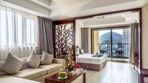 A hotel room with a sofa, a bed, a balcony with a view of buildings and mountains, and a decorative partition. - Sanya Baohong Shang Haihuating boutique hotel (Sanya)