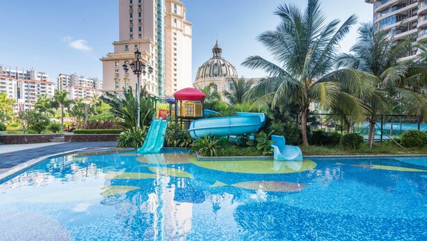 A swimming pool with slides and a water play area, surrounded by palm trees and buildings. - Sanya Baohong Shang Haihuating boutique hotel (Sanya)