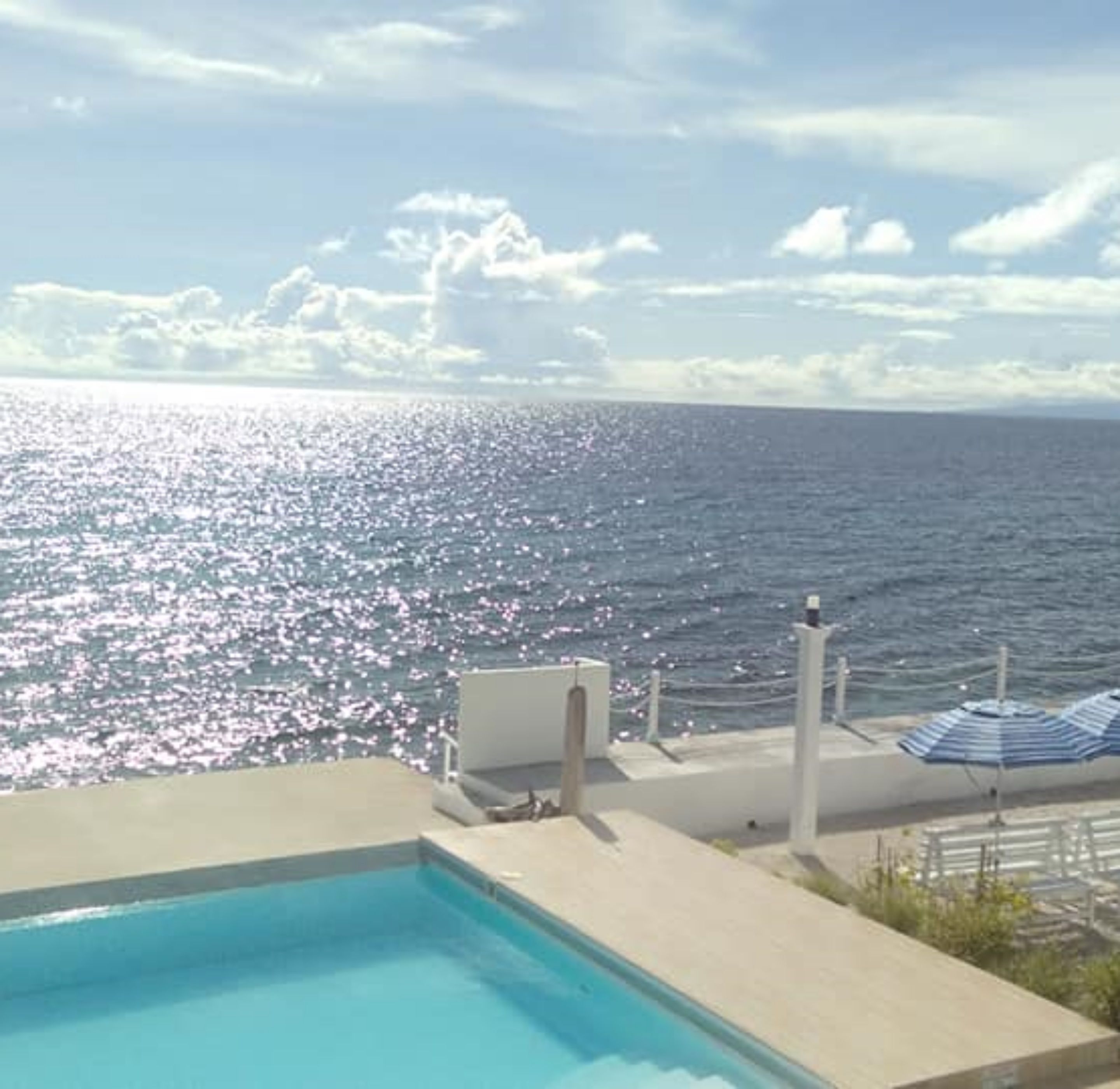 Ein Poolbereich mit Blick aufs Meer, eine Liege und ein Sonnenschirm.