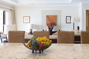 A modern living room with wicker furniture, a fruit bowl on the coffee table, and artwork on the walls.