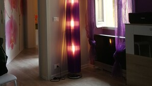 Ein Zimmer mit Holzboden, einer Stehlampe, einem Fenster mit violetten Vorhängen und einem weißen Klimagerät.