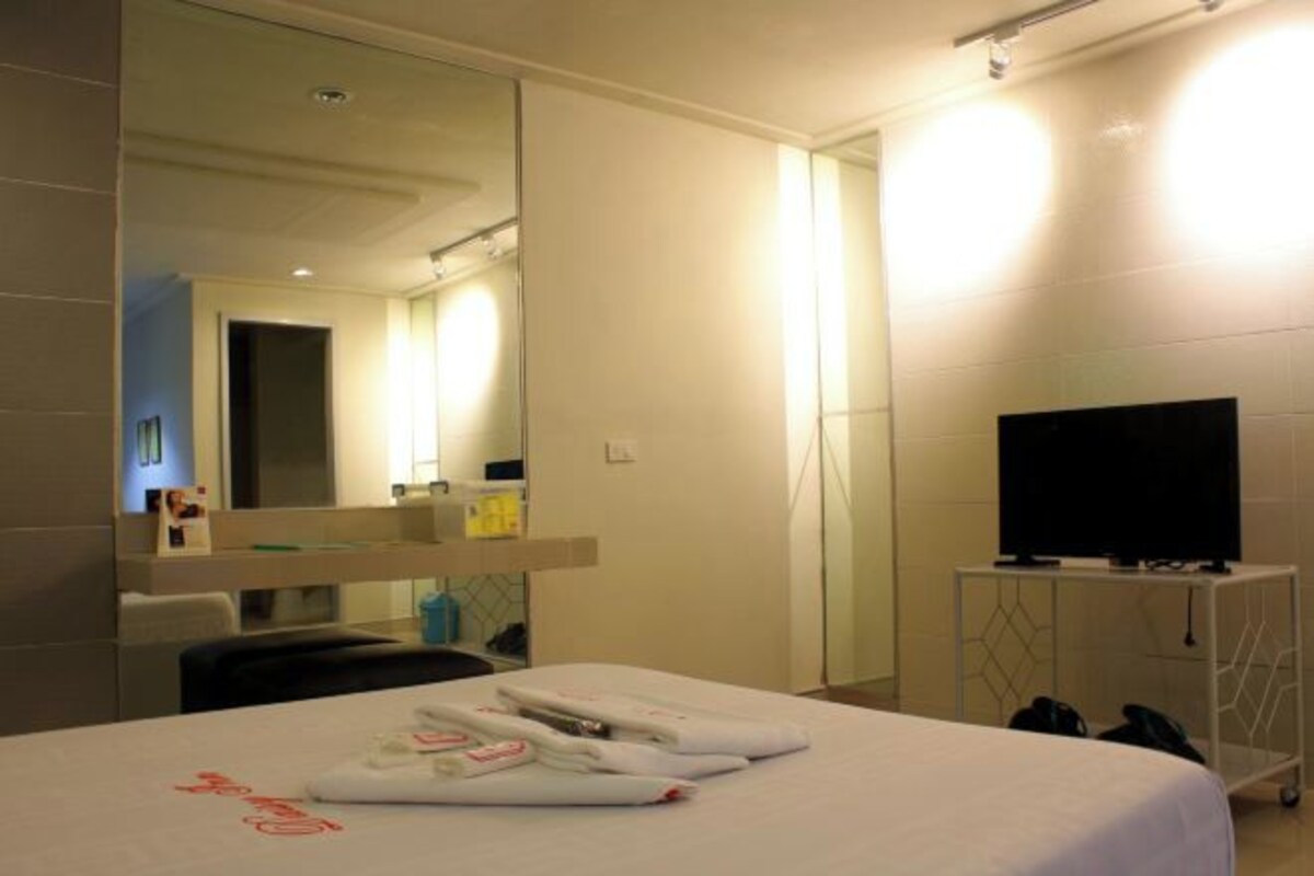 A hotel room with a bed, a television on a stand, a mirror, and a wall-mounted TV.