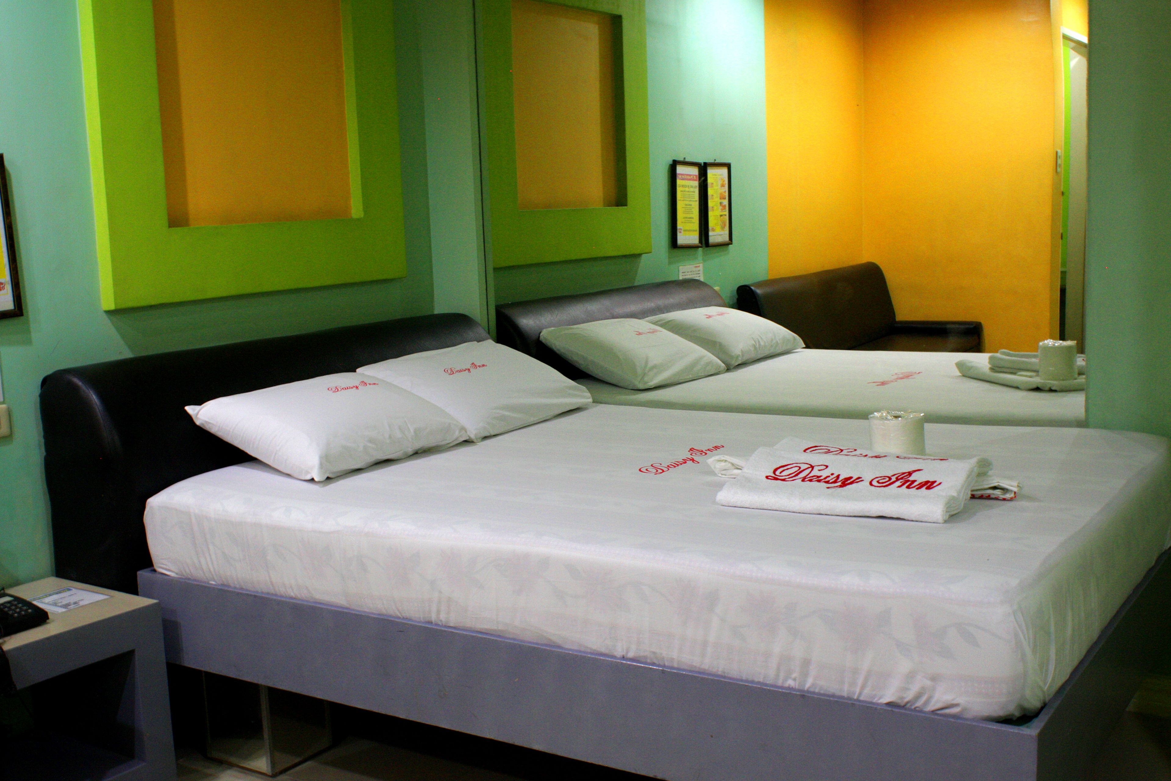 Habitación de hotel con dos camas, cada una con ropa blanca y almohadas, y una mesita con un control remoto.