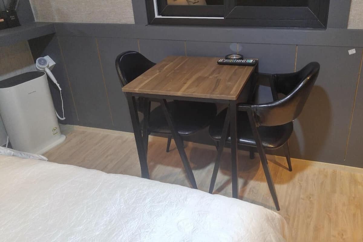 Um quarto pequeno com uma mesa de madeira e duas cadeiras pretas, uma cama com cobertura branca e uma janela com vista.
