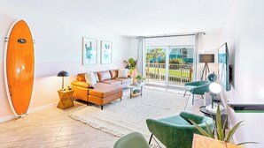 Een moderne woonkamer met een groot surfboard, een bank, een bijzettafeltje en een televisie.