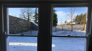 Et vindue med udsigt over et sneklædt landskab, inklusive en stenvæg og et træhegn.