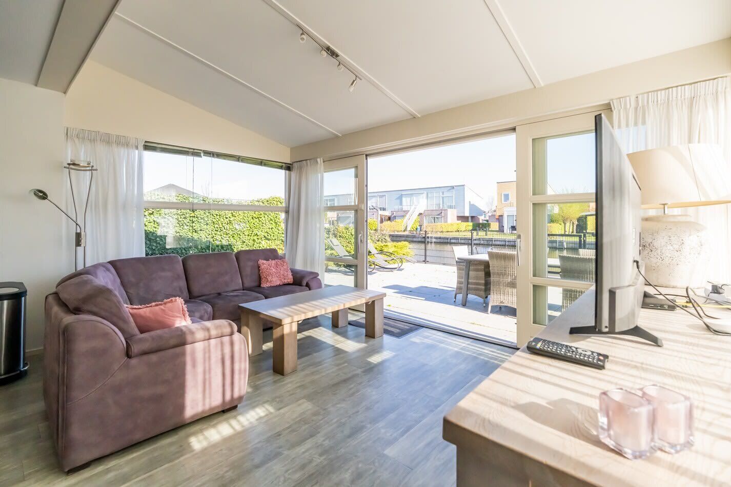 A modern living room with a sofa, a coffee table, and a desk with a computer. Large windows offer a view of the outside.