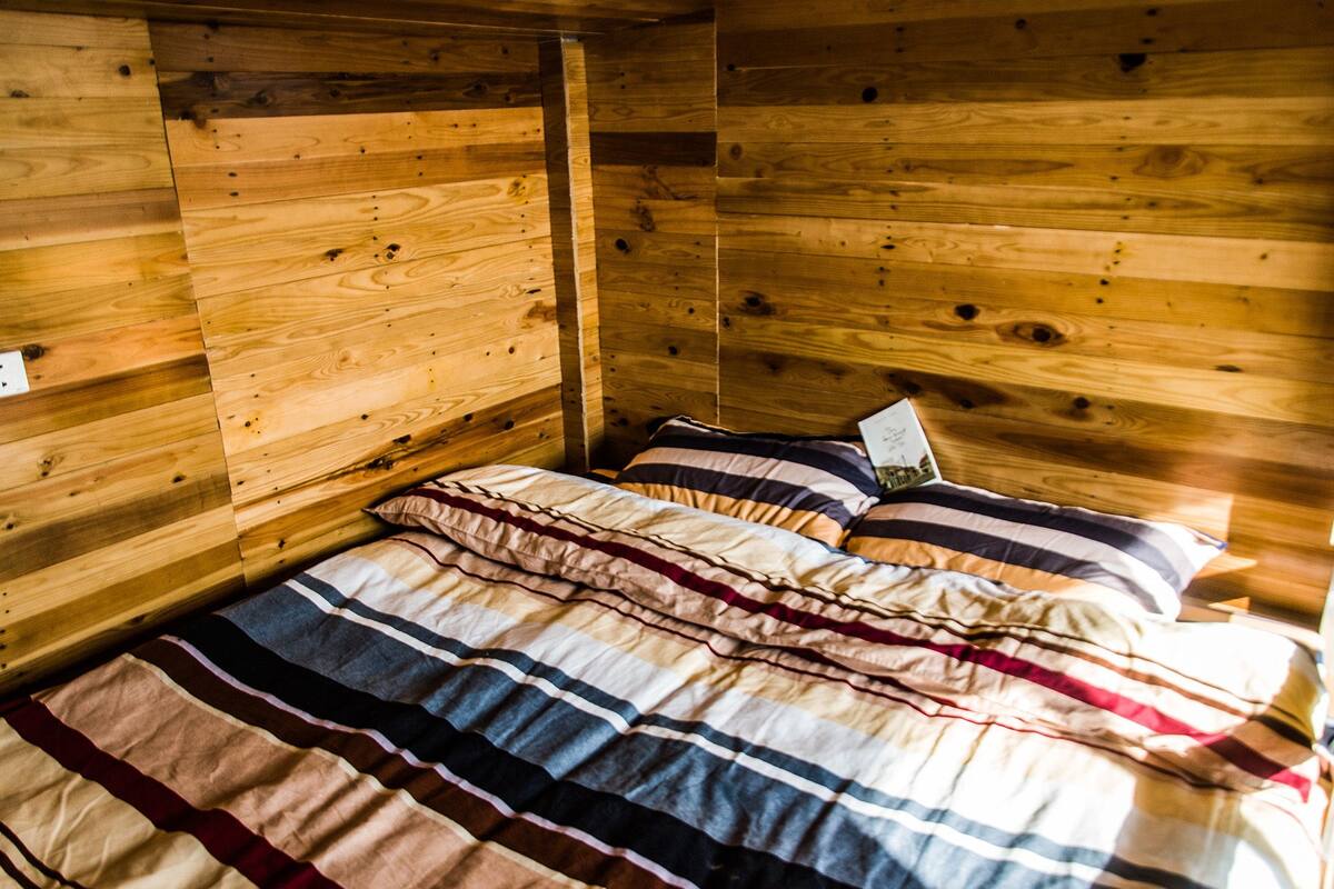 A wooden cabin room with a bed, striped bedding, and a book on the nightstand.