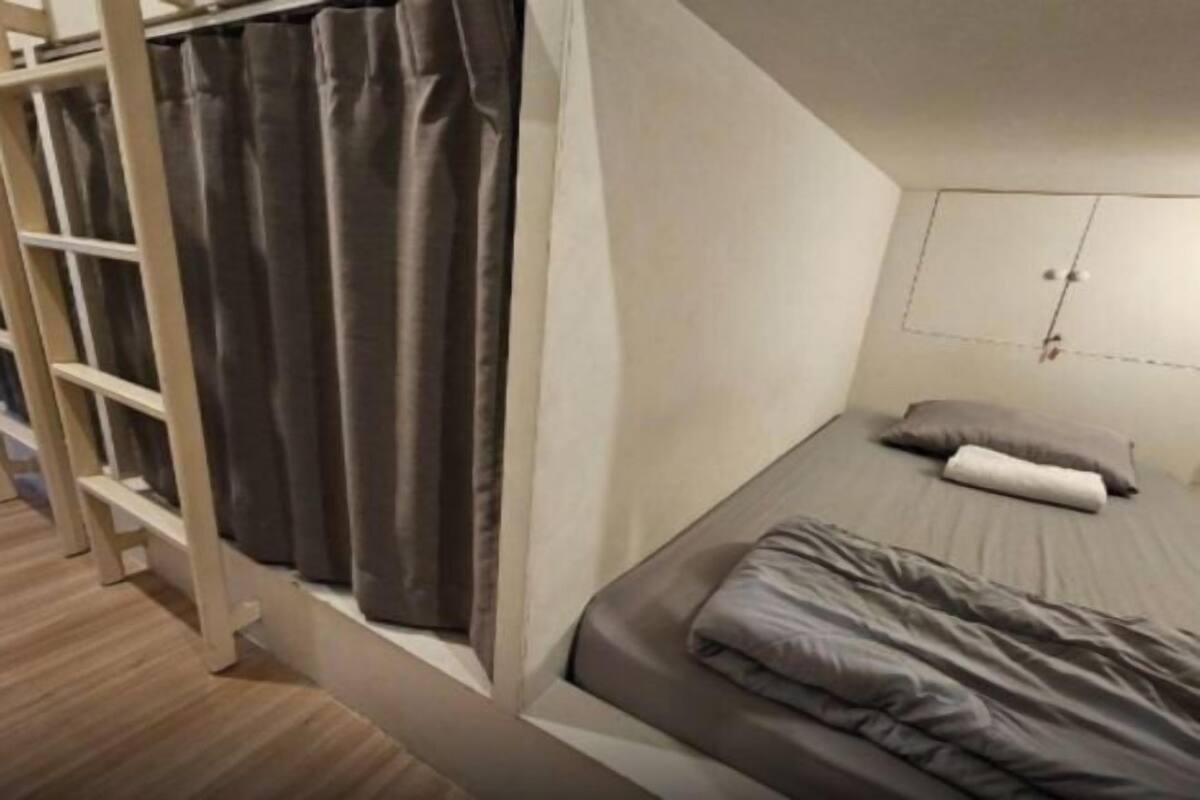 Une petite chambre avec un lit simple et un lit superposé en bois d’un côté, une armoire blanche et une couverture de lit grise.