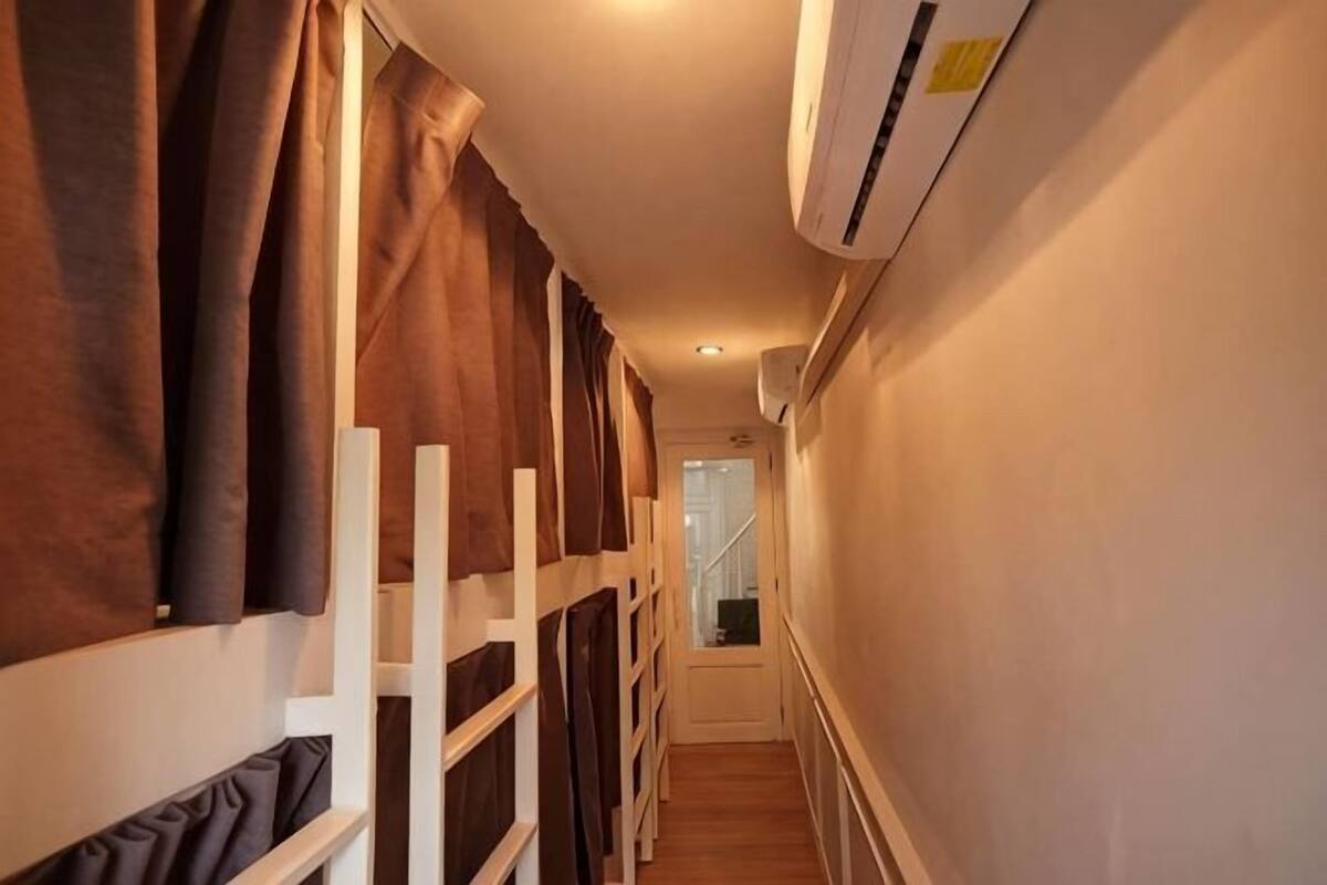 Un couloir étroit avec des lits superposés, un appareil de climatisation et un escalier en arrière-plan.