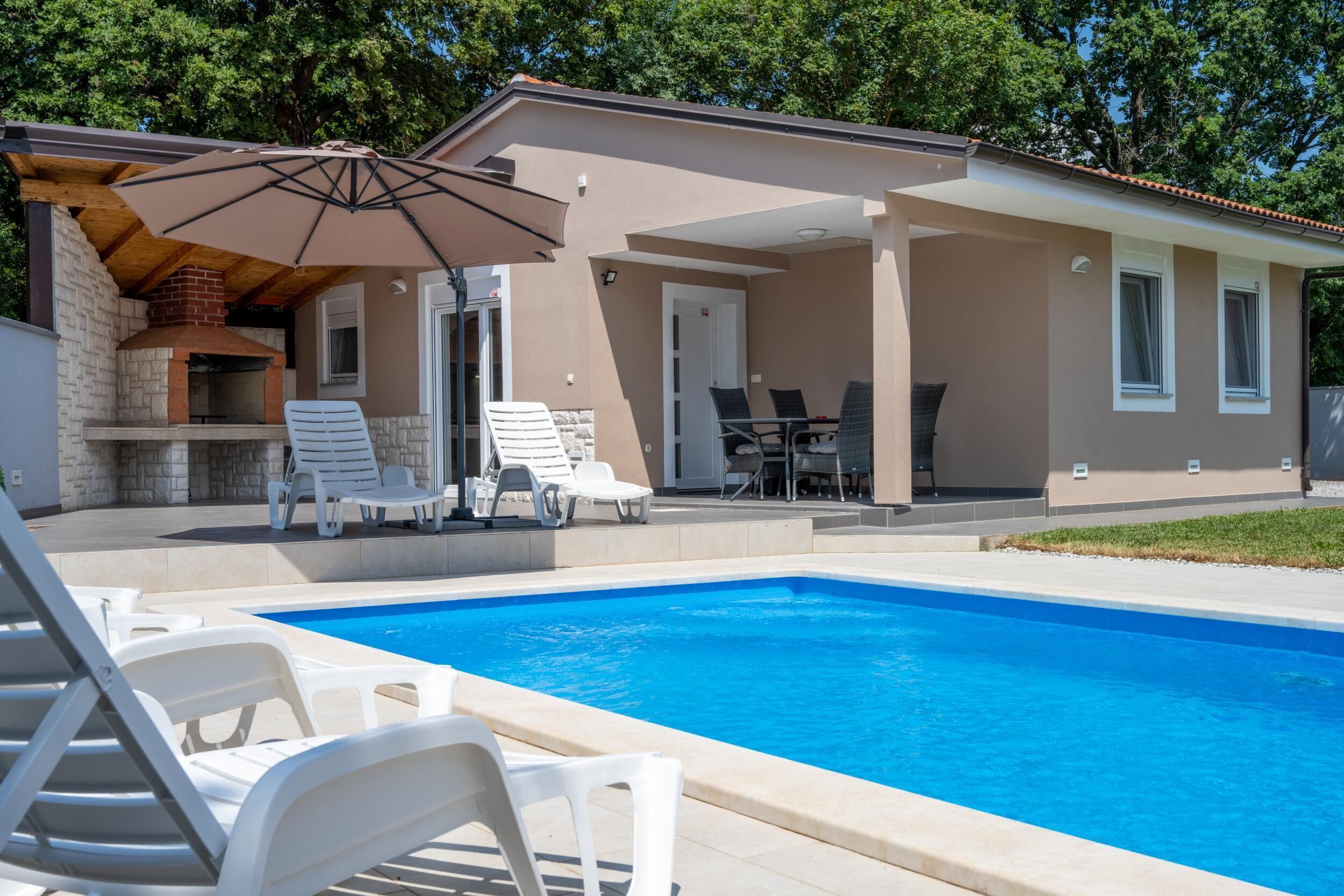 A poolside area with a barbecue, lounge chairs, and a covered patio.